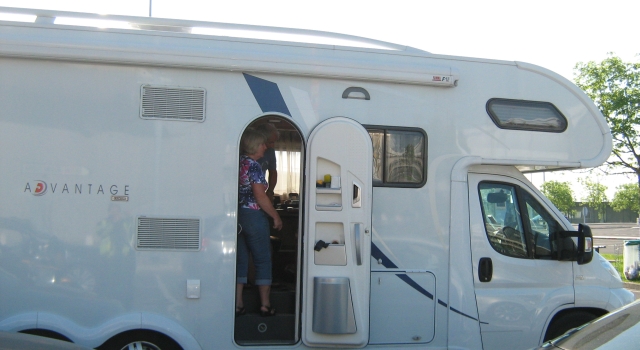 a large white campervan in the sunshine with a lady stood in the doorway